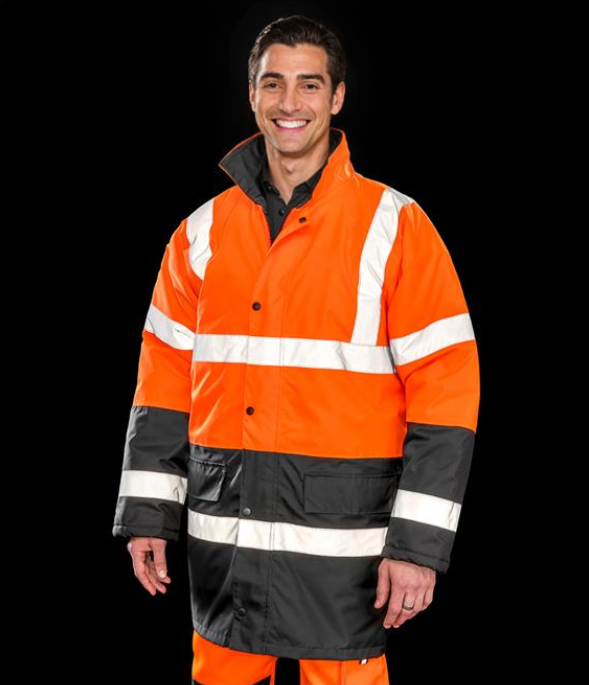 A person wearing a Result Core Motorway Two Tone Safety Jacket in orange and black with reflective bands and a concealed hood.